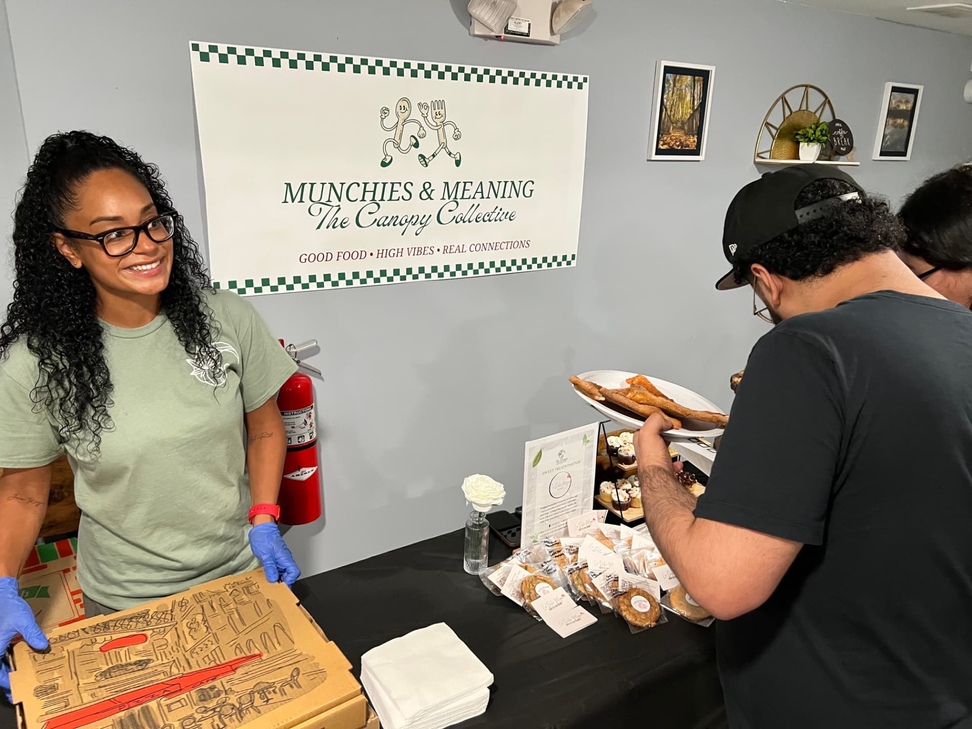 A community member holding a box of comfort food in front of the Munchies & Meaning sign.